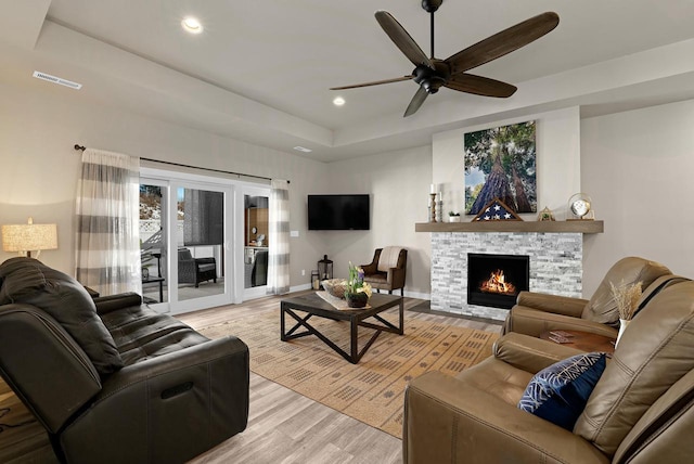 living area with a tray ceiling, light wood-style flooring, a fireplace, and visible vents