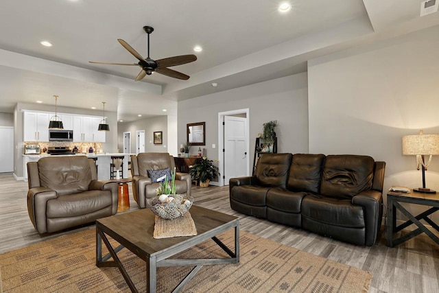 living area with a ceiling fan, a raised ceiling, recessed lighting, and visible vents