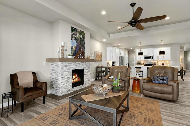 living room with recessed lighting, baseboards, a stone fireplace, and light wood finished floors