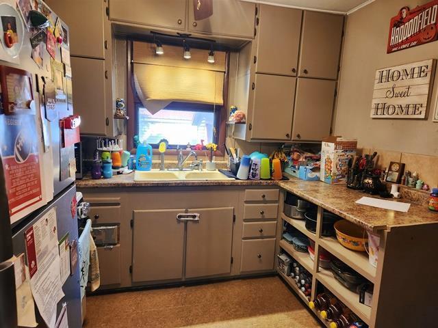 kitchen featuring gray cabinetry, light countertops, freestanding refrigerator, and a sink