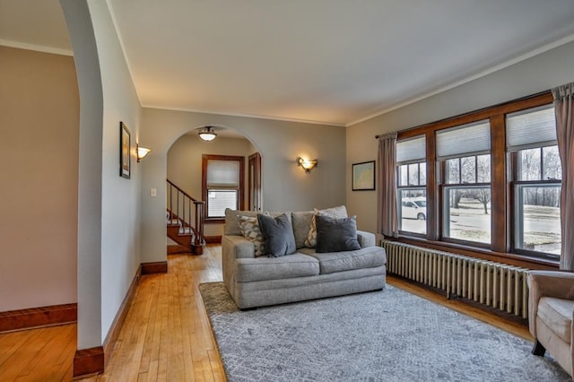 living area with baseboards, light wood finished floors, radiator heating unit, arched walkways, and stairs