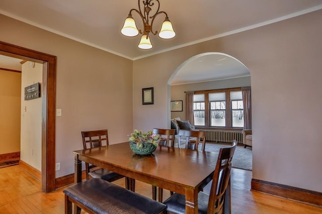 dining area featuring crown molding, radiator heating unit, arched walkways, and light wood finished floors