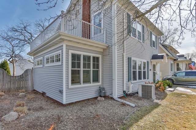 view of side of property with central AC unit, a balcony, and fence