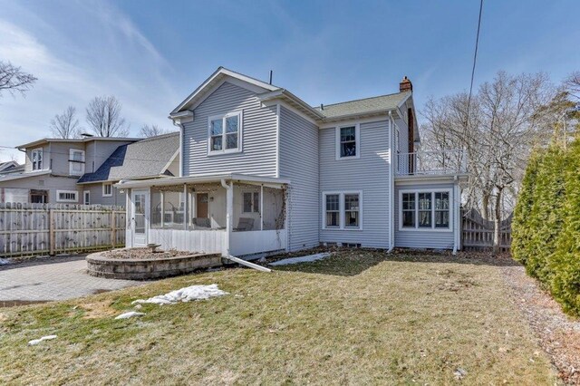 back of property featuring fence, a chimney, a balcony, a sunroom, and a yard