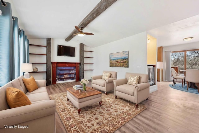 living area featuring ceiling fan, a fireplace, lofted ceiling with beams, and light wood-style floors