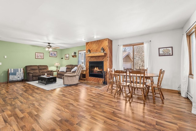 living room featuring ceiling fan, baseboards, a large fireplace, and wood finished floors