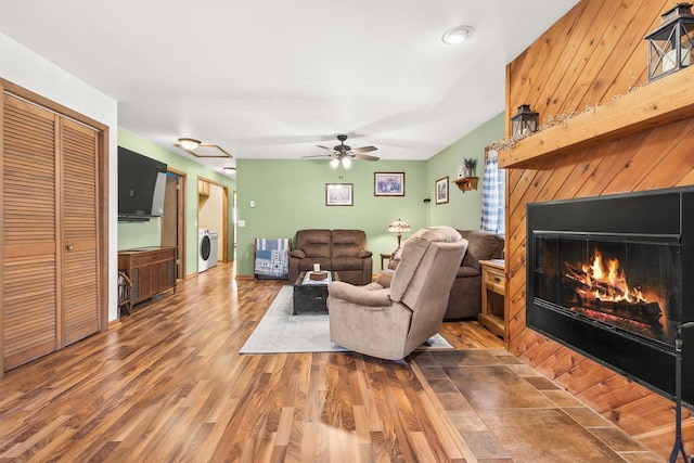 living area featuring ceiling fan, a lit fireplace, and wood finished floors