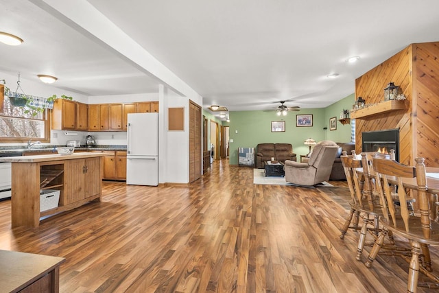 kitchen featuring open floor plan, freestanding refrigerator, light wood-style floors, a glass covered fireplace, and a ceiling fan