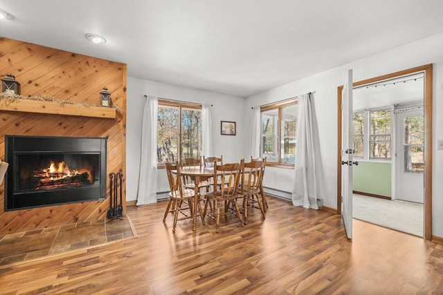 dining space featuring a glass covered fireplace, a baseboard radiator, baseboards, and wood finished floors