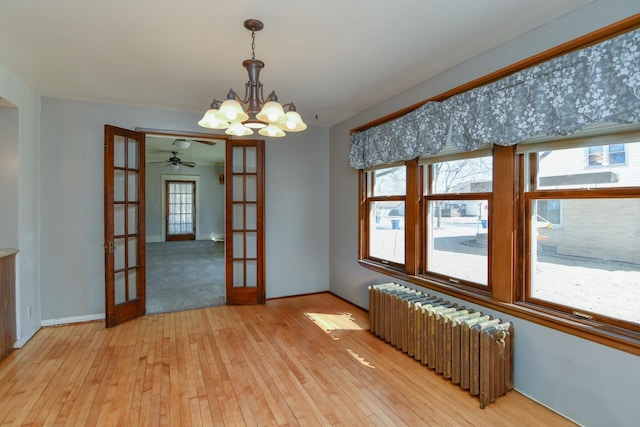 empty room with baseboards, a chandelier, radiator heating unit, french doors, and light wood-style floors