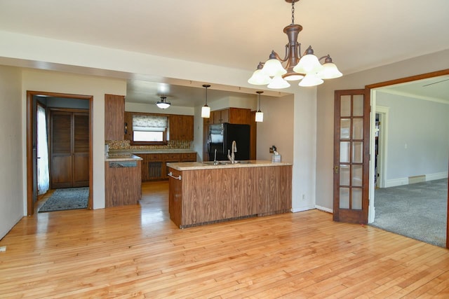 kitchen featuring light wood finished floors, a chandelier, a peninsula, freestanding refrigerator, and brown cabinetry