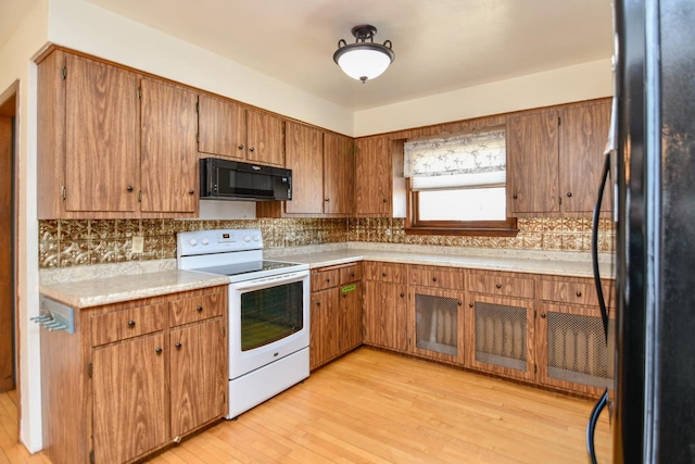 kitchen featuring black appliances, tasteful backsplash, light wood-style floors, brown cabinetry, and light countertops