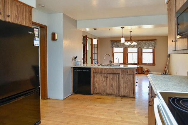 kitchen with a peninsula, a sink, black appliances, light countertops, and brown cabinets