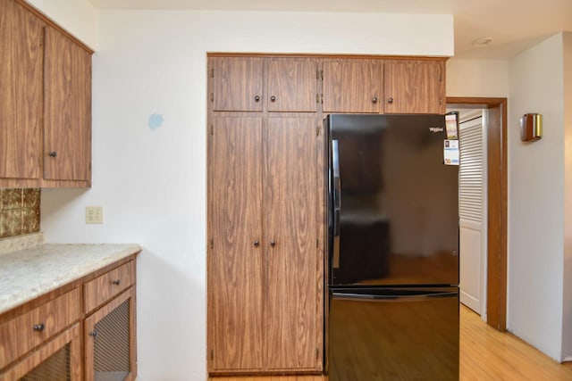 kitchen with light countertops, light wood-style floors, brown cabinets, and freestanding refrigerator