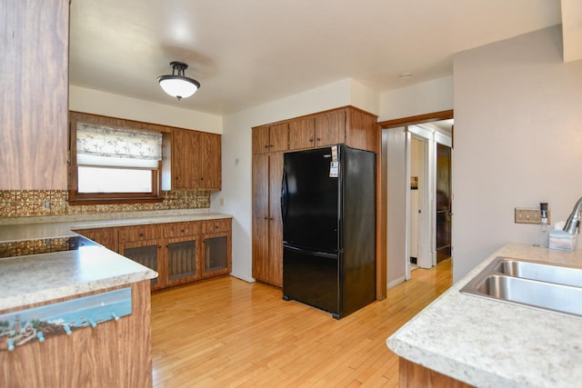 kitchen with brown cabinetry, freestanding refrigerator, a sink, decorative backsplash, and light wood-type flooring