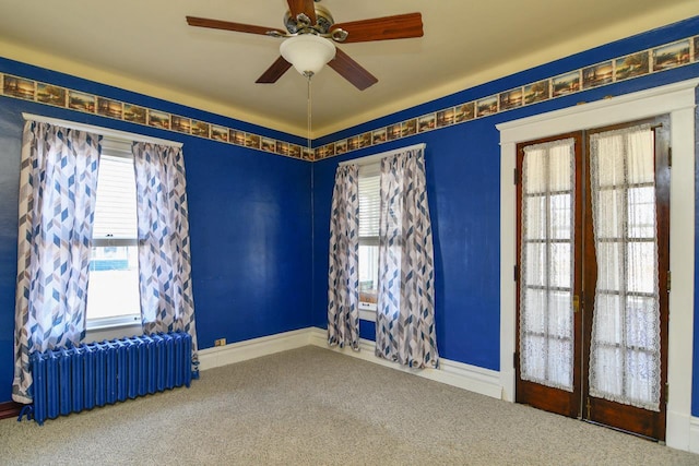 carpeted empty room with baseboards, plenty of natural light, radiator, and ceiling fan