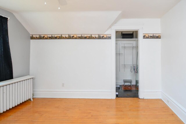 unfurnished room with radiator, a ceiling fan, wood finished floors, baseboards, and lofted ceiling