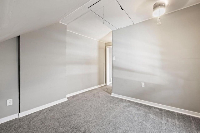 carpeted spare room featuring attic access, baseboards, and lofted ceiling