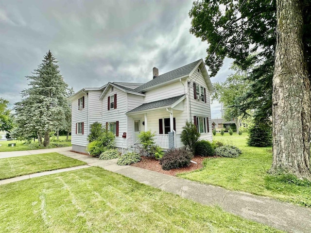 view of front facade featuring covered porch, a chimney, a front yard, and a shingled roof