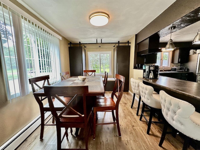 dining space with a baseboard heating unit, a barn door, and light wood finished floors