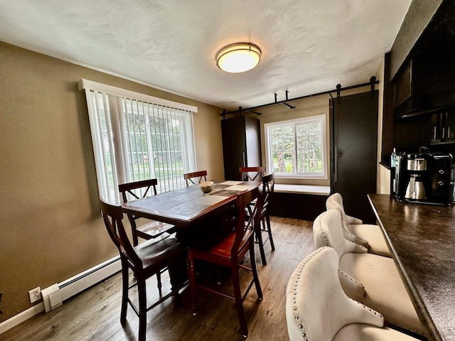 dining room featuring plenty of natural light, baseboards, a barn door, and wood finished floors