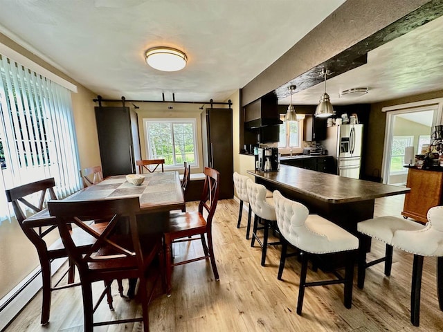 dining room featuring a barn door, baseboard heating, and light wood finished floors