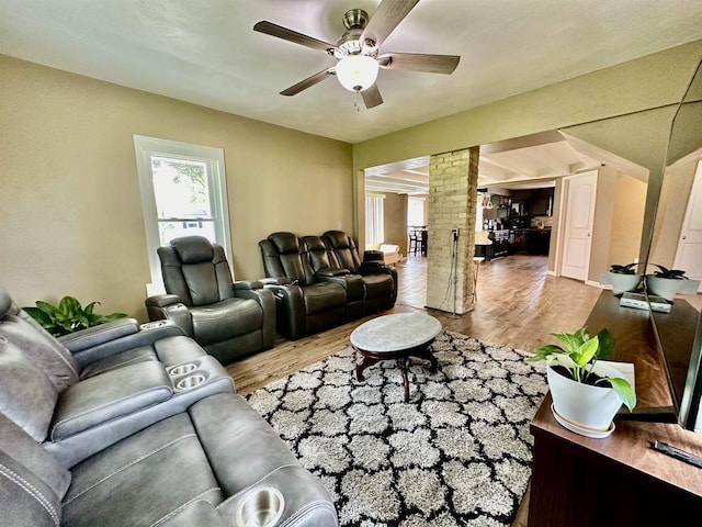 living area with decorative columns, wood finished floors, and a ceiling fan