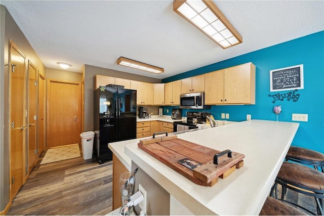 kitchen featuring light brown cabinets, a peninsula, black appliances, light countertops, and a kitchen breakfast bar