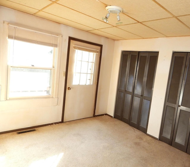 unfurnished bedroom with visible vents, baseboards, carpet, multiple closets, and a paneled ceiling