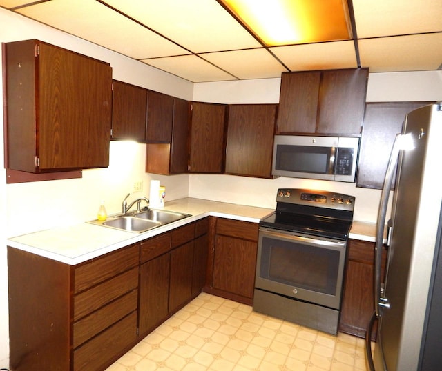 kitchen with light floors, a drop ceiling, a sink, light countertops, and appliances with stainless steel finishes