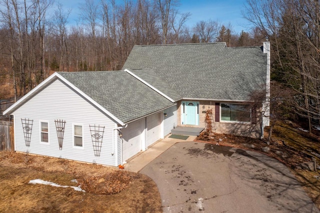 view of front of house with a chimney, an attached garage, a shingled roof, and driveway