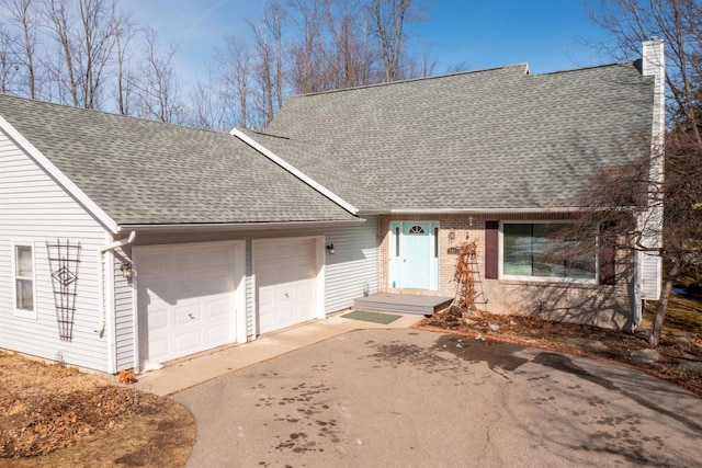 view of front facade featuring driveway, roof with shingles, a garage, brick siding, and a chimney