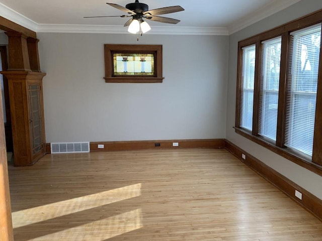 empty room featuring visible vents, light wood-style flooring, crown molding, decorative columns, and baseboards