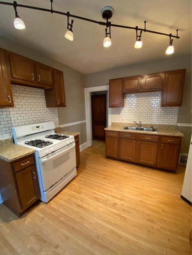 kitchen with a sink, light wood-style flooring, white gas stove, and decorative backsplash