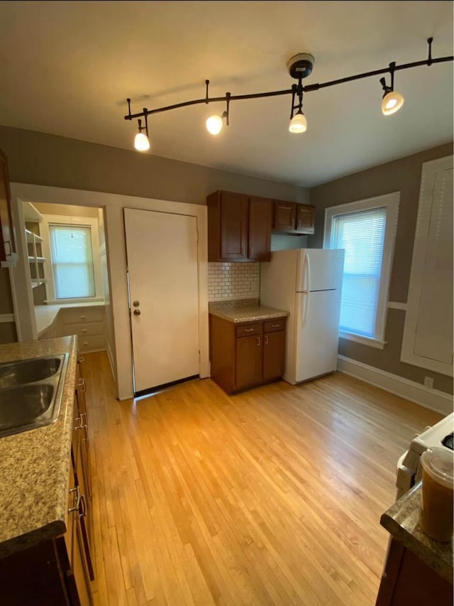 kitchen featuring tasteful backsplash, light wood-style flooring, brown cabinets, freestanding refrigerator, and a sink