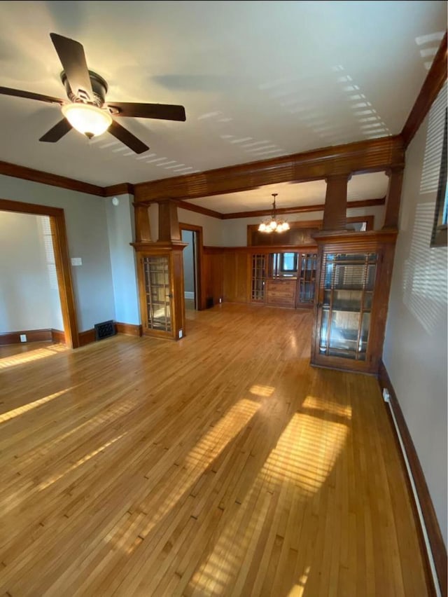 unfurnished living room featuring ceiling fan with notable chandelier, hardwood / wood-style flooring, crown molding, and baseboards