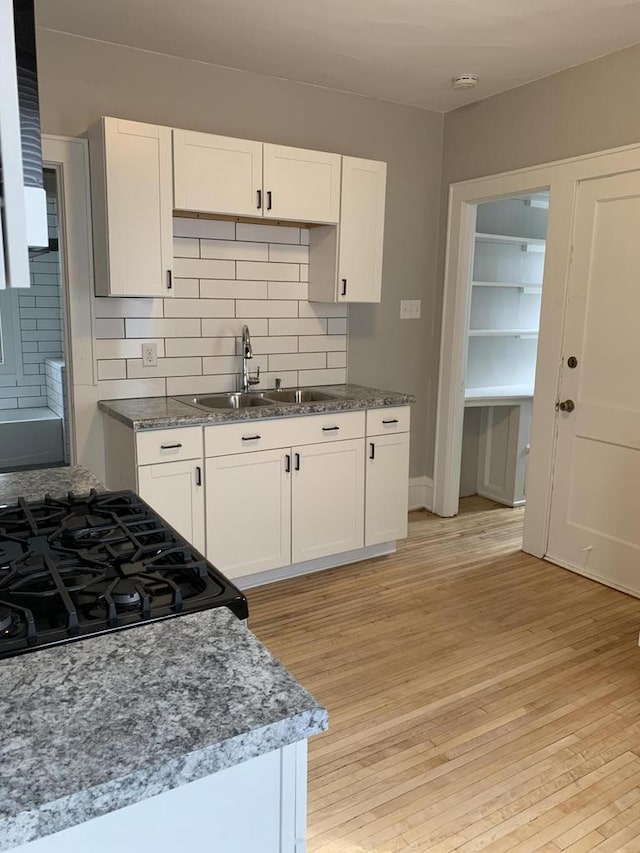 kitchen with light wood finished floors, backsplash, black gas range, white cabinetry, and a sink