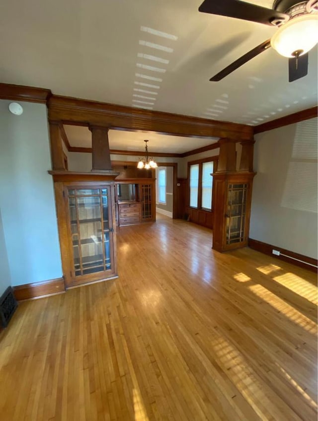 unfurnished living room featuring ceiling fan with notable chandelier, baseboards, wood-type flooring, and ornamental molding