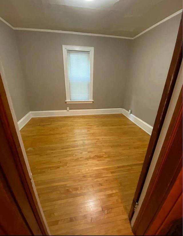 empty room with crown molding, light wood-type flooring, and baseboards