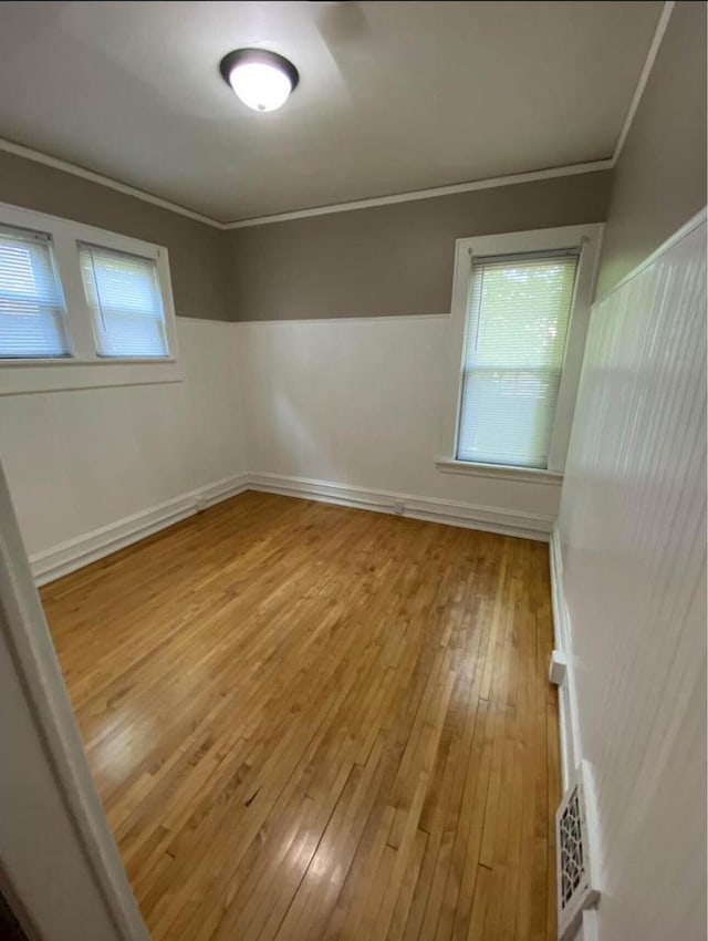 spare room with a wealth of natural light, visible vents, light wood-style floors, and crown molding