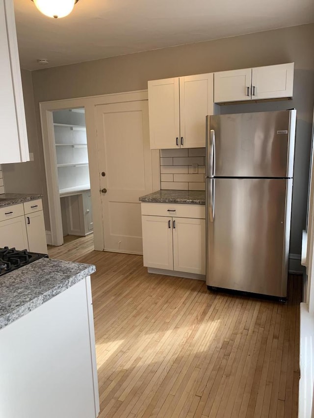 kitchen featuring backsplash, white cabinets, light wood finished floors, and freestanding refrigerator