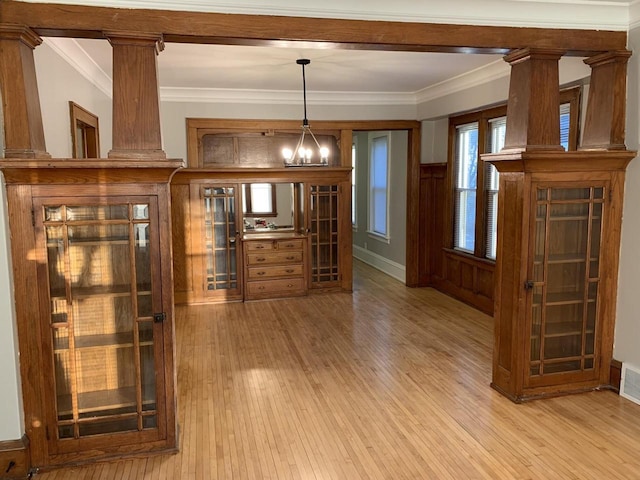 bar featuring a notable chandelier, light wood-style floors, ornamental molding, and ornate columns