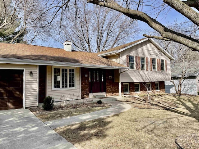 tri-level home with an attached garage, a chimney, and roof with shingles