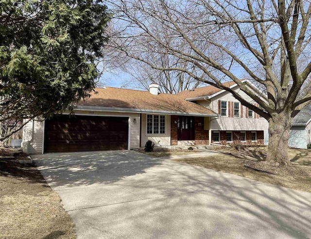 tri-level home with brick siding, a shingled roof, concrete driveway, a chimney, and an attached garage