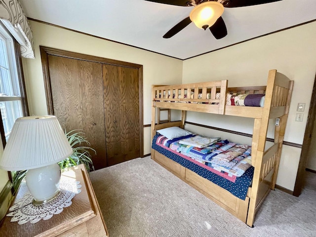 carpeted bedroom featuring crown molding, a closet, and ceiling fan