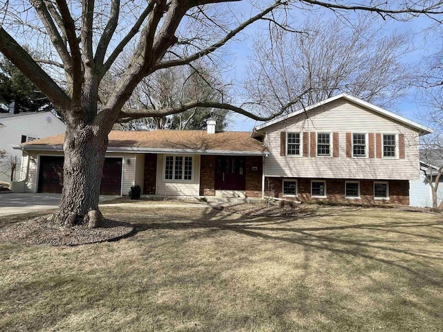 split level home with a front yard, driveway, a chimney, a garage, and brick siding