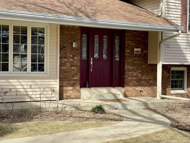 view of exterior entry featuring brick siding, a porch, and roof with shingles