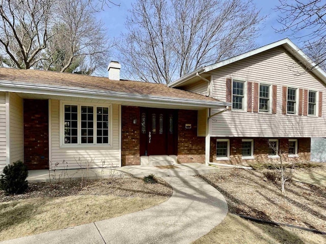 split level home with brick siding, a porch, and a chimney