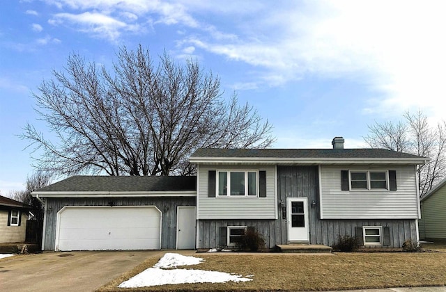 bi-level home with a front lawn, a garage, driveway, and a chimney