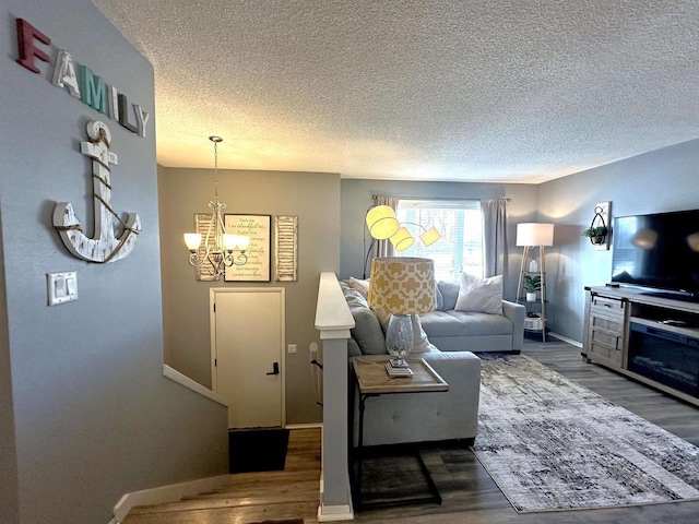 living room with a notable chandelier, baseboards, a textured ceiling, and wood finished floors